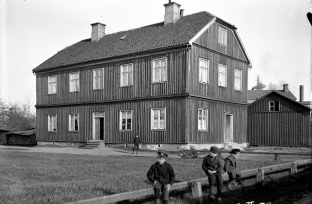 old picture of a building with children sitting on a fence